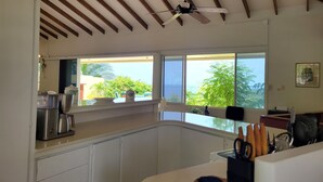 A kitchen with white cabinets, a ceiling fan, and large windows overlooking greenery.