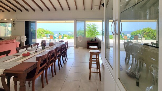 A dining area with a long wooden table, chairs, and a view of the ocean.