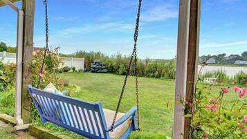 A blue wooden swing chair suspended by chains, set in a covered outdoor area with a grassy lawn and a view of a residential neighborhood.