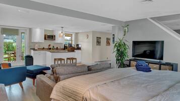 A modern, open-plan living space with a large bed, seating area, kitchenette, and a TV.