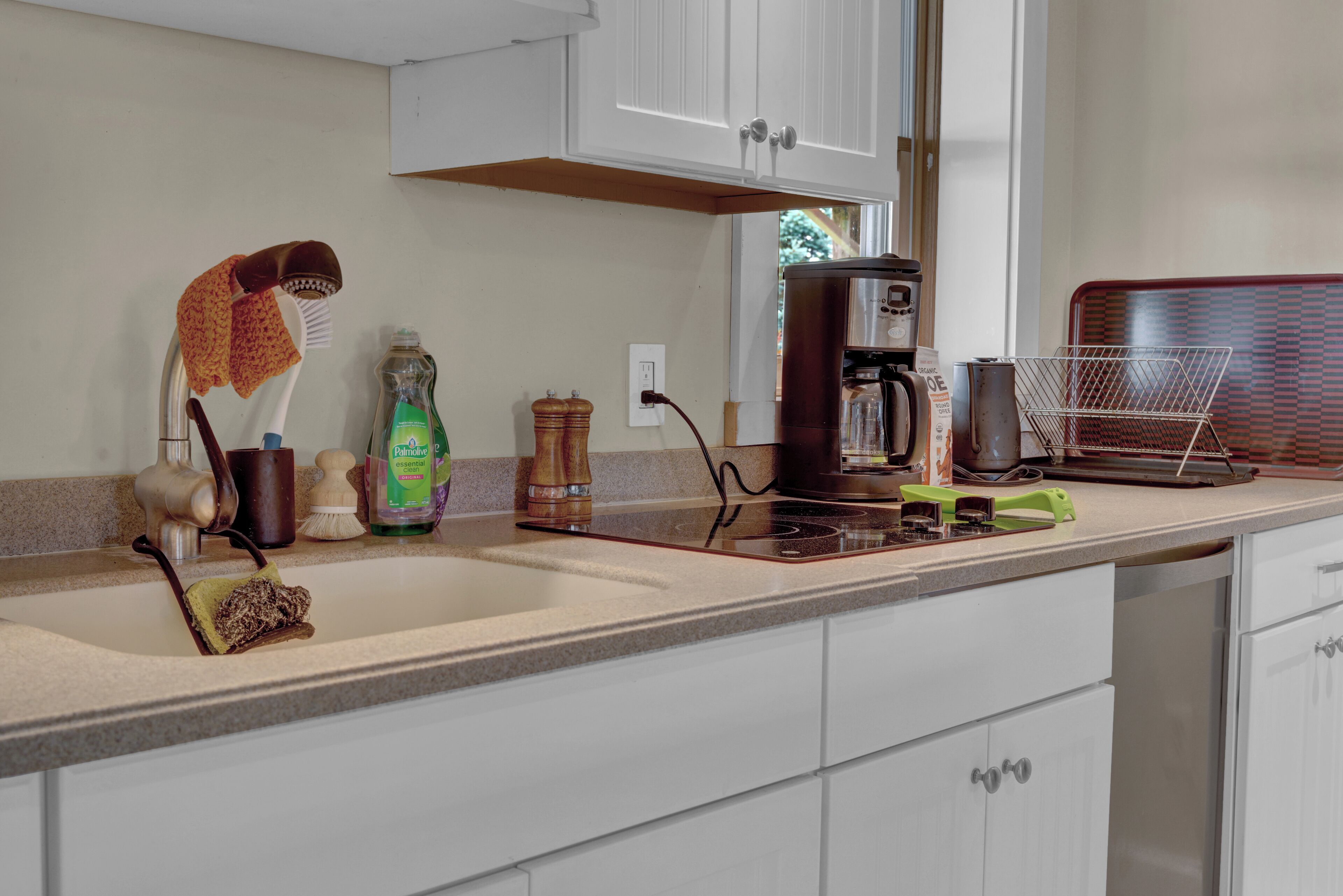 A kitchen with white cabinets, a coffee maker, a kettle, and various kitchen utensils.