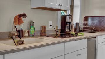 A kitchen with white cabinets, a coffee maker, a kettle, and various kitchen utensils.