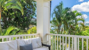 Ein Balkon mit weißer Couch, weißem Geländer und üppiger tropischer Bepflanzung im Hintergrund.