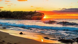 Ein Strand mit Wellen, einem Sonnenuntergang und einer felsigen Klippe.