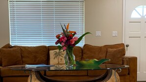 A living room with a brown sofa, a glass coffee table, and a vase of flowers. - Fabulous 3-bedroom Hawaiian home. (Waimea)