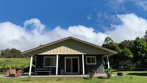 A single-story building with a gabled roof, a covered porch with benches, and a large window. - Fabulous 3-bedroom Hawaiian home. (Waimea)