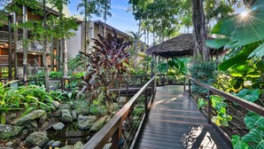 A wooden bridge connecting two buildings with a tropical garden on either side.