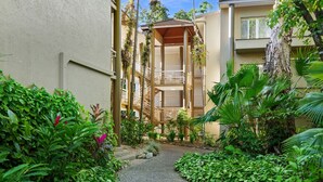 A courtyard with a wooden pergola, lush greenery, and a building with a balcony.