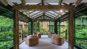 A covered outdoor seating area with wicker furniture and glass walls.