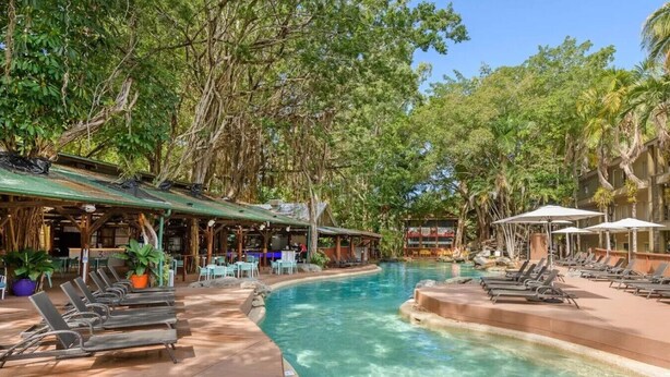 A pool area with lounge chairs, a bar, and a covered seating area surrounded by trees.