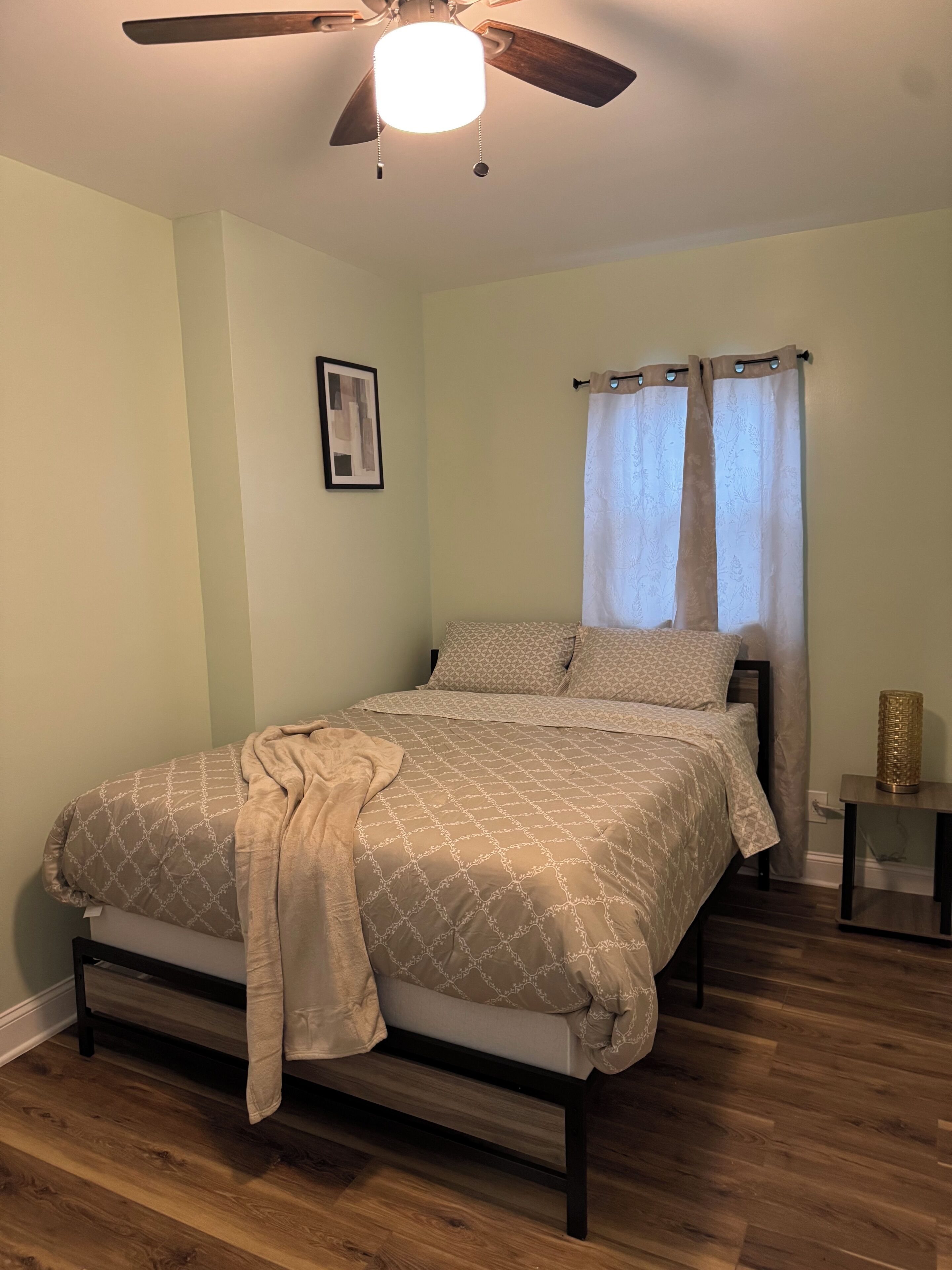 A bedroom with a bed, a ceiling fan, a nightstand, and a window with curtains.