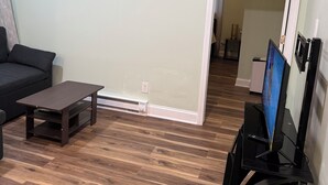 A living room with a dark brown wooden floor, a black TV stand with a flat-screen TV, a dark brown coffee table, and a black sofa. - Amazing 2-bedroom apartment with AC in Philadelphia (Philadelphia)