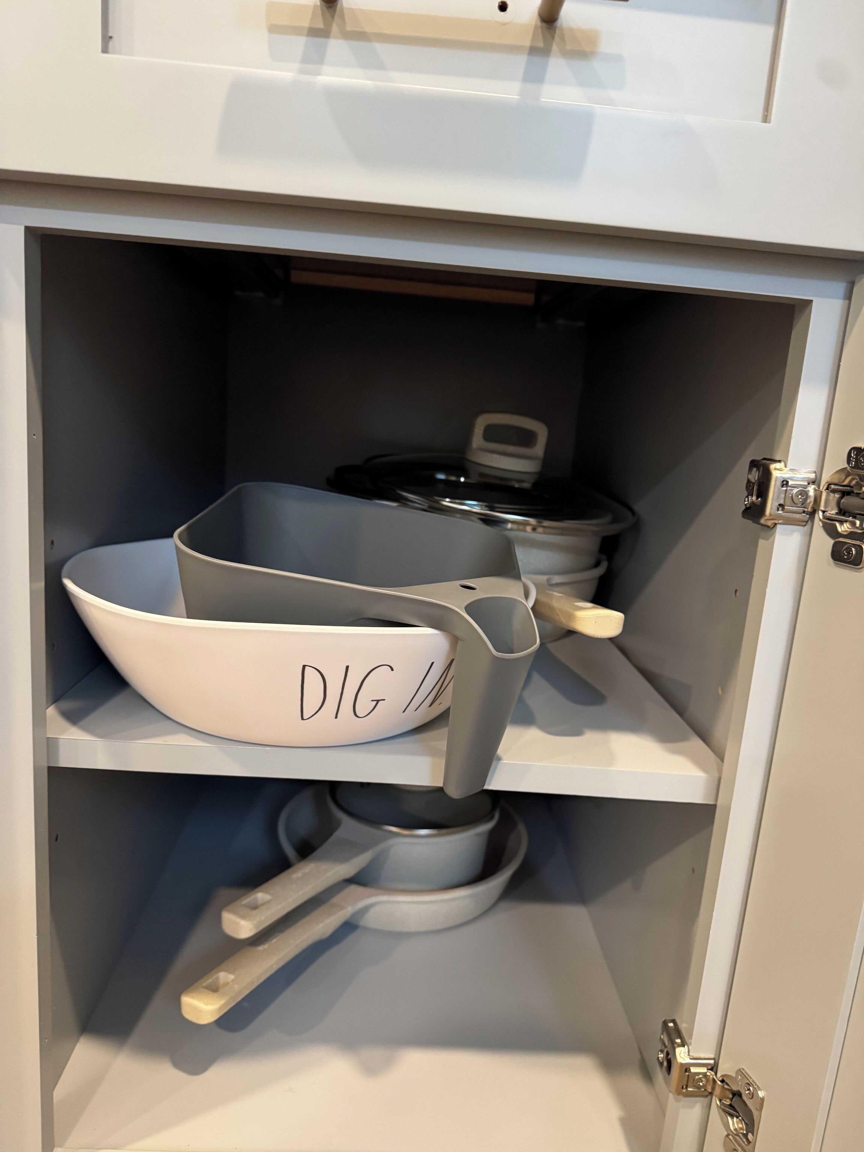 Un armario de cocina con interior blanco, que contiene diversos utensilios de cocina, incluyendo un cuenco blanco etiquetado con “DIG” y una olla.