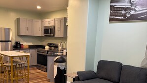 A modern living room with a grey sofa, a small table, and a kitchen area with grey cabinets and a microwave. - Amazing 2-bedroom apartment with AC in Philadelphia (Philadelphia)
