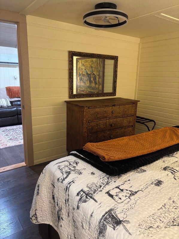 A bedroom with a bed, a wooden dresser, a framed picture, and a door leading to a balcony.