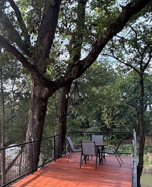 An outdoor deck with a table and chairs, surrounded by trees.