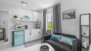 A compact living space with a kitchenette, a sofa with cushions, a coffee table, and a window with curtains. - Coconut cabana, freshly renovated unit September 2025 heated pools (Clearwater)