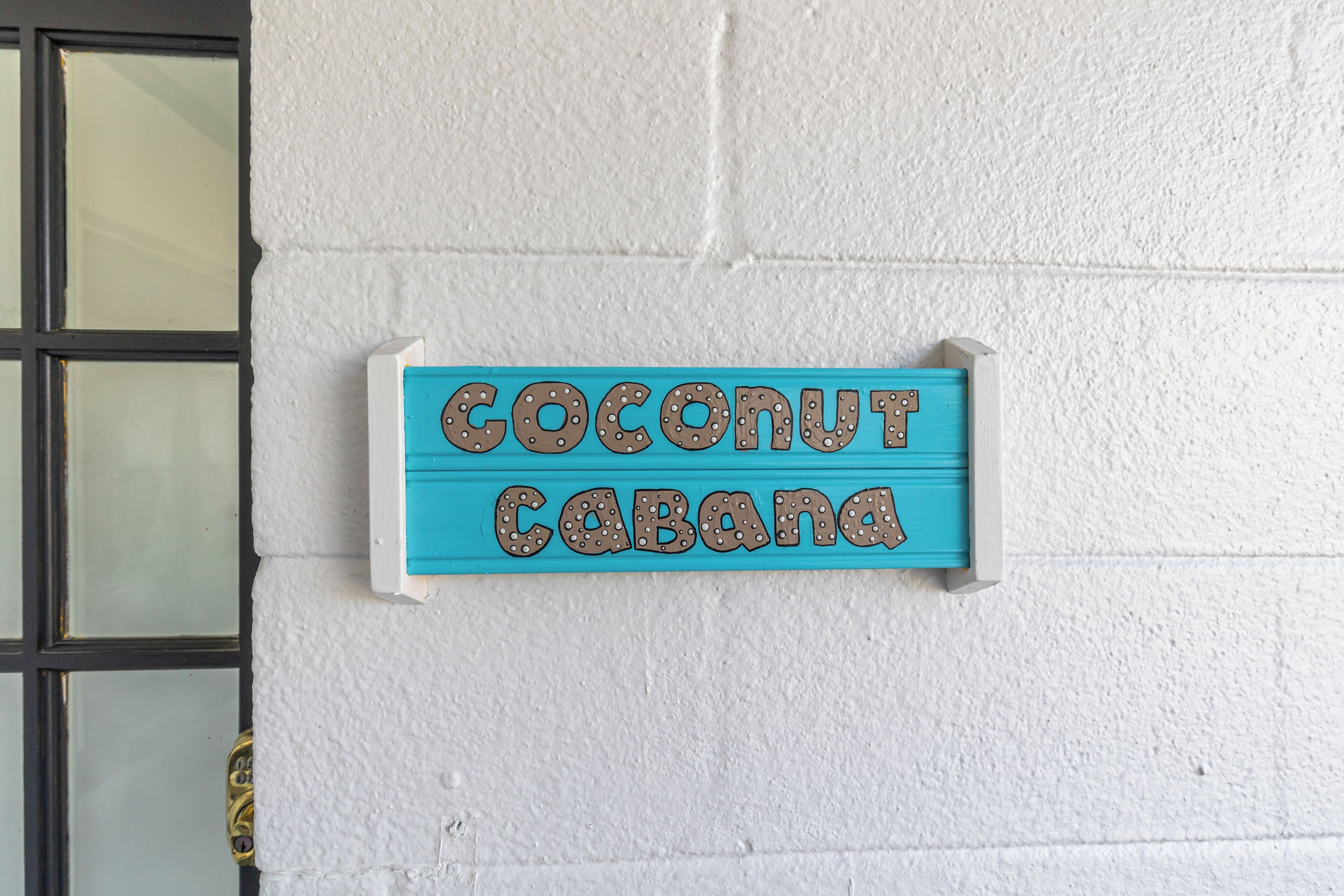Una señal en una pared blanca que dice 'Coconut Cabana'.