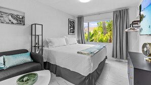 A modern hotel room with a bed, a sofa, a desk, and a large window with curtains. - Coconut cabana, freshly renovated unit September 2025 heated pools (Clearwater)