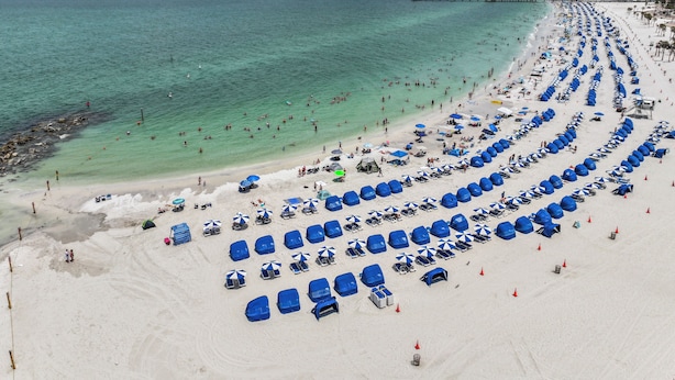 A beach with rows of blue umbrellas and beach chairs, a pier extending into the water, and a clear sky. - Coconut cabana, freshly renovated unit September 2025 heated pools (Clearwater)
