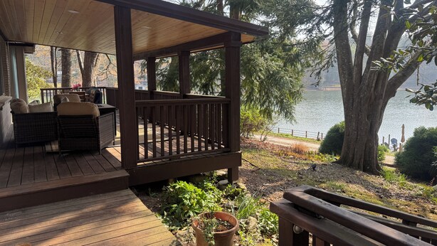 Eine Holzterrasse mit Gartenmöbeln, mit Blick auf einen See.