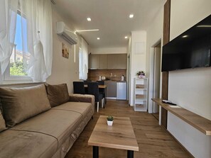 A compact living space with a sofa, a small dining table, a kitchen area, and a TV mounted on the wall.