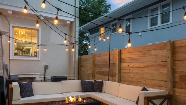 Una zona d'estar exterior acollidora amb un sofà modular, una xemeneia i llums penjants.