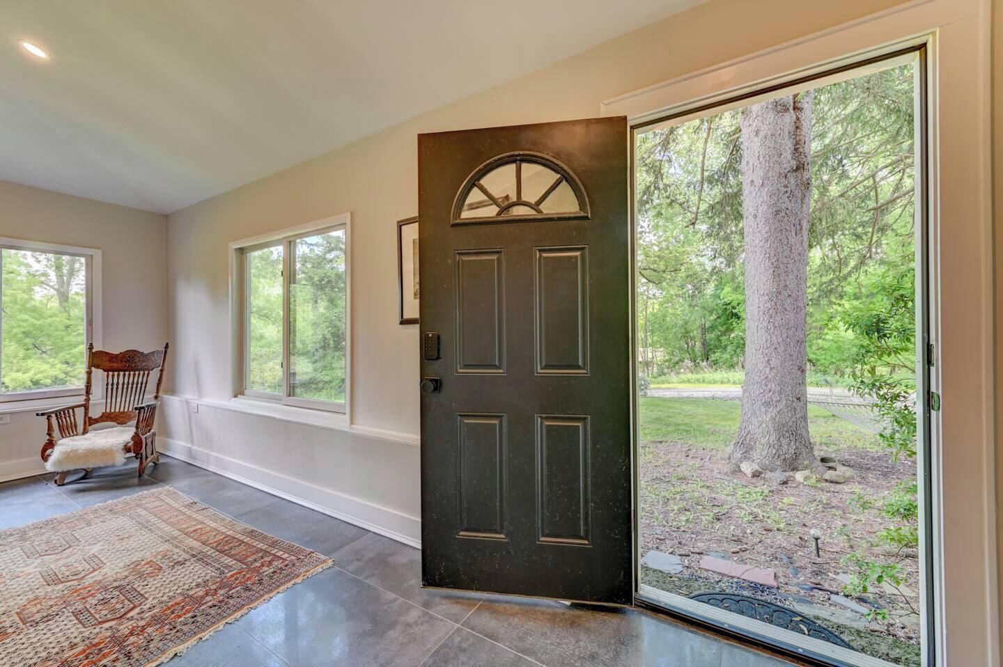 A modern entryway with a dark wooden door, large windows, and a rug leading to a chair.
