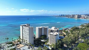 Un hotel costero con varios edificios altos, un aparcamiento y vistas al océano y la playa.