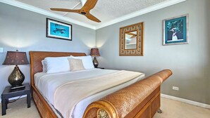 Un dormitorio con una cama de madera, dos mesitas de noche con lámparas, un ventilador de techo y cuadros enmarcados en las paredes.