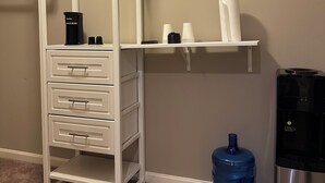 A compact room with a white storage unit, a water dispenser, and a coffee maker.