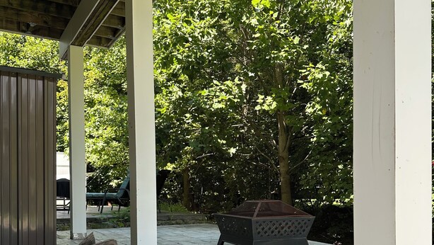 A covered patio area with stone flooring, wooden beams, and a fire pit.