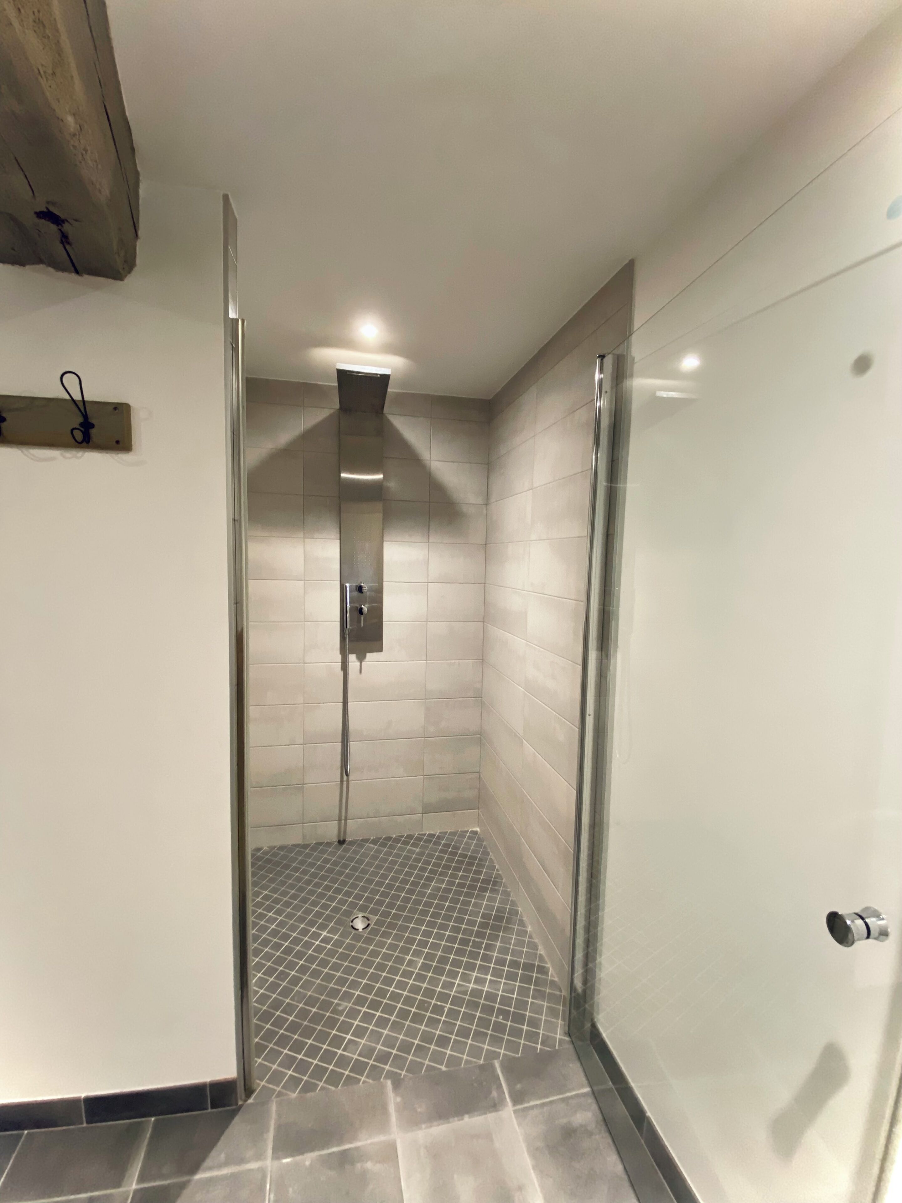 A modern shower area with a glass door, tiled walls, and a metal showerhead.