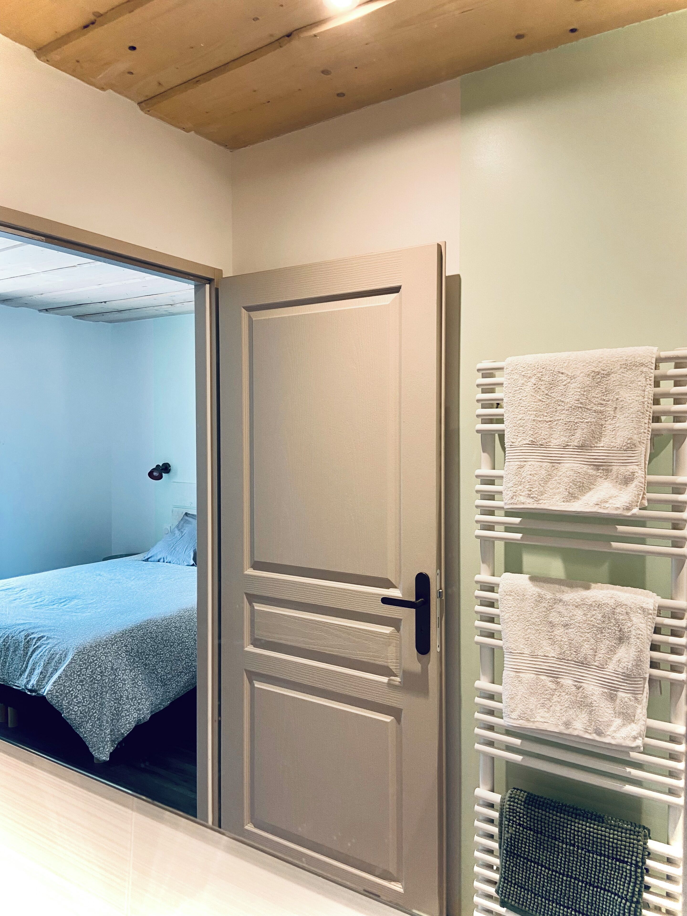 Een kamer met een schuifdeur, een bed, een witte handdoekhouder met handdoeken en een houten plafond.