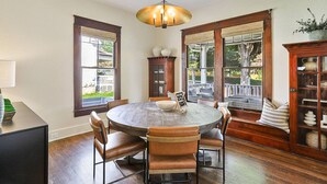 Un comedor con una mesa redonda de madera, sillas de cuero, una araña y vistas al exterior a través de amplios ventanales.