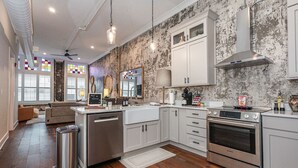 Una cocina moderna con armarios blancos, electrodomésticos de acero inoxidable y un salpicadero con diseño de piedra desgastada.