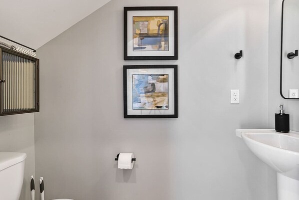 Une salle de bain équipée de toilettes, d’un lavabo et de deux œuvres d’art encadrées accrochées au mur.