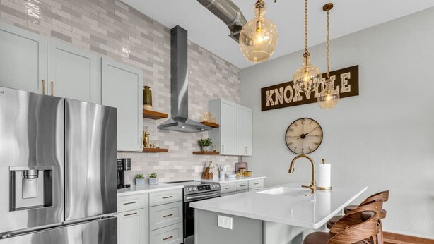A modern kitchen with stainless steel appliances, a central island with bar stools, a clock, and a 'Knoxville' sign on the wall.