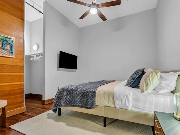 Un dormitorio con cama, ventilador de techo, televisor montado y pared de madera.