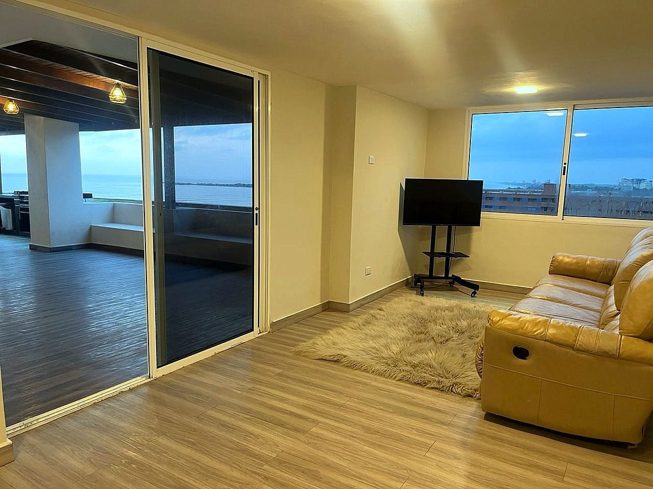 A living room with a sofa, a television, and a view of the sea through a sliding glass door.