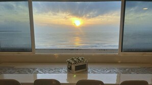 A table with a floral centerpiece and four chairs, positioned in front of a window with a view of the sunset over the water. - Espectacular Penthouse con Terraza Privada ! (Tucacas)