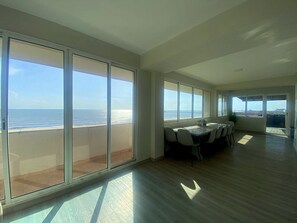 Una habitación amplia con ventanas grandes, una zona de comedor con sillas y vistas a la playa.