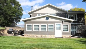 Une maison à deux étages avec un porche à l’avant, des fondations en pierre et une grande pelouse.