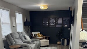 Un salon moderne avec un canapé d’angle gris, une petite table d’appoint en bois et un tapis à motifs.