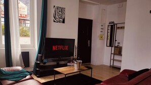 A living room with a large flat-screen TV displaying 'NETFLIX', a leather sofa, a coffee table, and a bookshelf. - Glamorous flat in Mertzwiller (Mertzwiller)