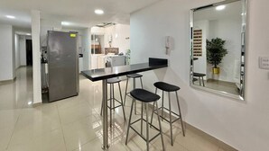 A modern kitchen with a stainless steel refrigerator, a black countertop, and three bar stools. - Medellín Poblado Gem • Steps to Cafés & Nightlife (Medellín)