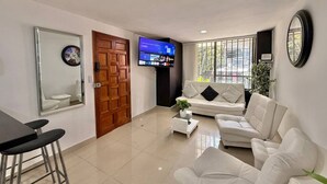 A living room with a sofa, a coffee table, a TV, and a mirror. - Medellín Poblado Gem • Steps to Cafés & Nightlife (Medellín)