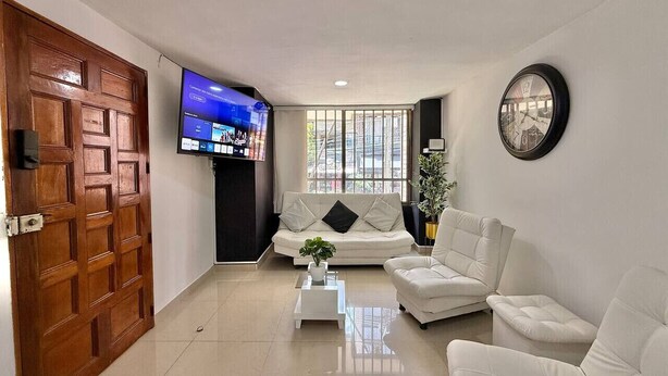 A living room with a sofa, a coffee table, a TV, and a clock on the wall. - Medellín Poblado Gem • Steps to Cafés & Nightlife (Medellín)