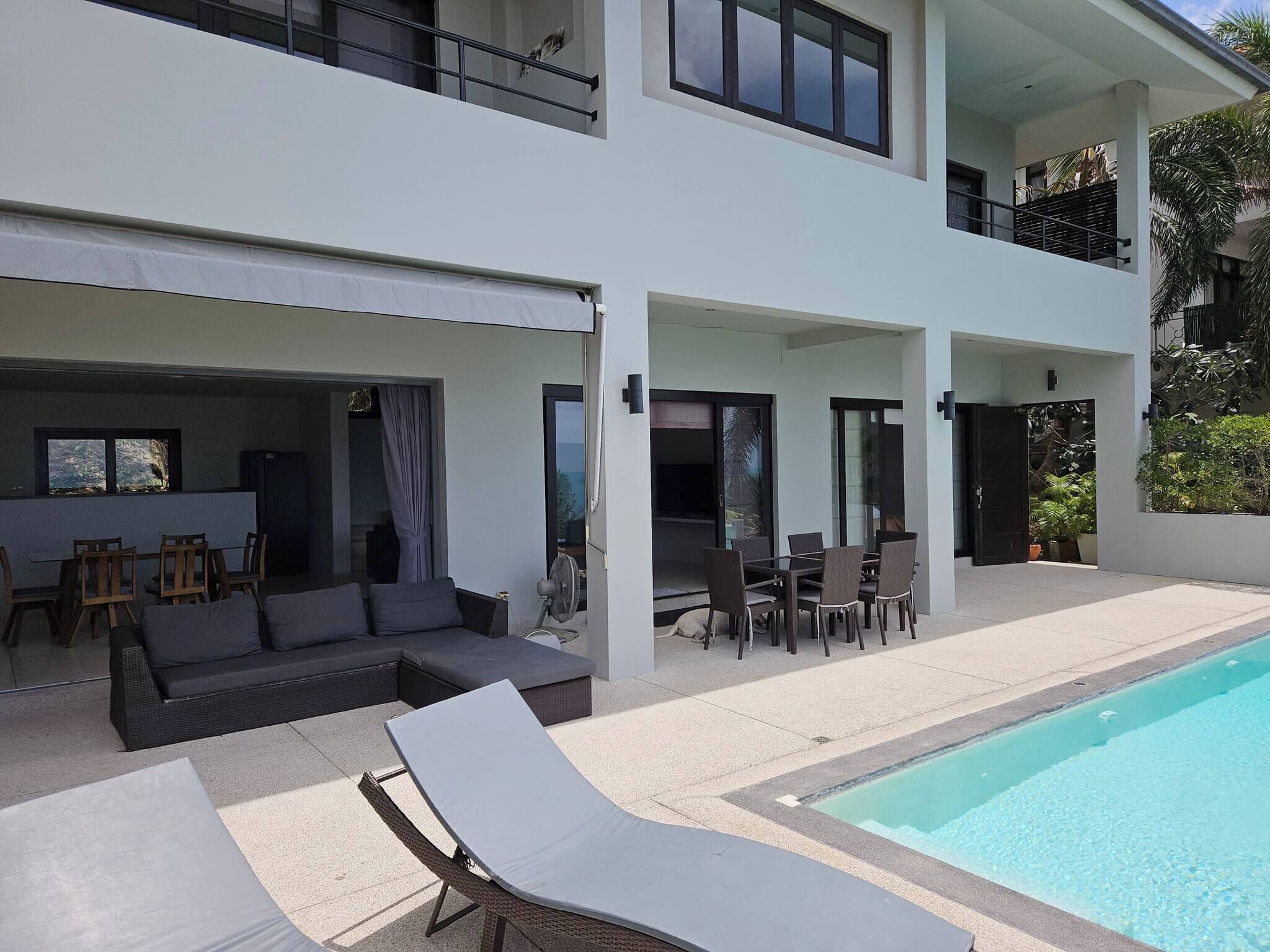 A modern two-story house with a swimming pool, outdoor seating, and a covered patio area.