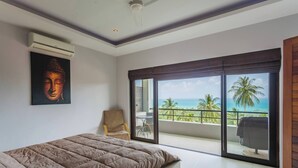 A bedroom with a large bed, a chair, a Buddha painting, and a balcony with a view of the sea and palm trees. - Serene Bay View Villa in Ko Samui - Your Tropical Paradise (Koh Samui)
